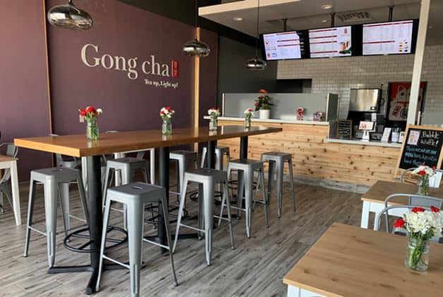 Photo of interior Gong cha store with purple walls, metal stools, and wooden tables.