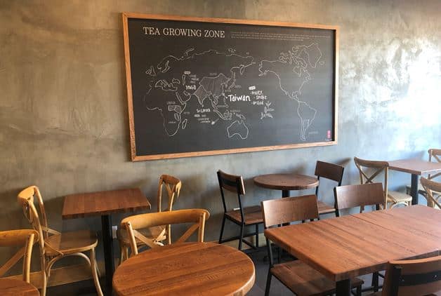 Photo of Gong cha store interior with wooden tables and chairs and chalkboard wall map